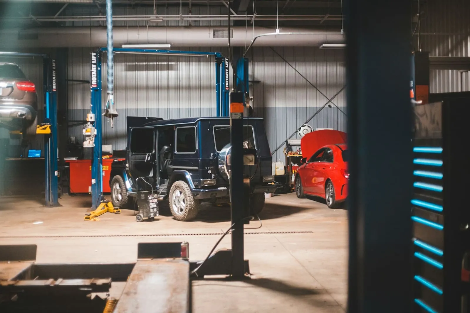 Interior de un taller mecánico con elevadores, un todoterreno con las puertas abiertas y un coche con el capó levantado